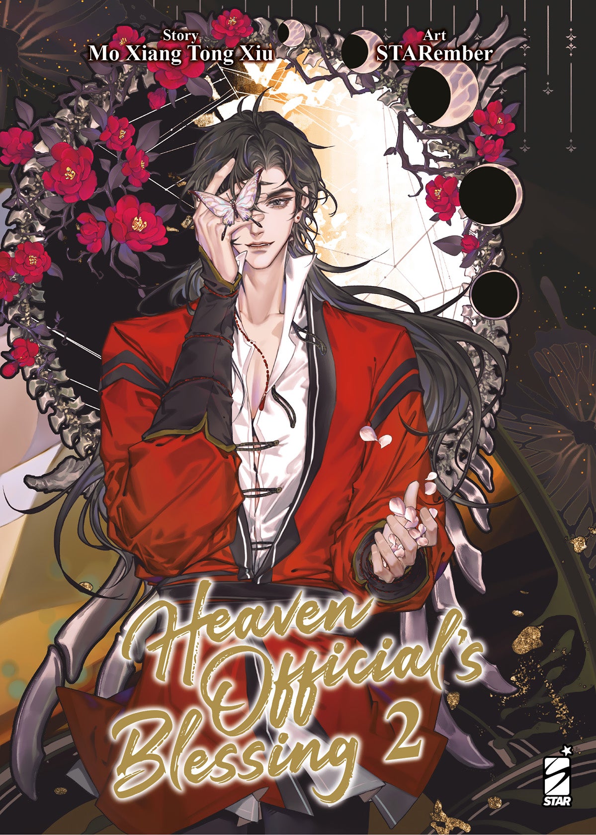 Copertina del manhua Heaven Official's Blessing Vol. 2, edito in Italia da Star Comics. L'illustrazione ritrae in primo piano l'affascinante Hua Cheng, un giovane dai lunghi e mossi capelli scuri, che indossa una ricca veste rossa con dettagli neri sopra una camicia bianca aperta sul petto. Con la mano destra, avvolta in un bracciale nero e rosso, tiene delicatamente una farfalla traslucida dai contorni violacei proprio davanti al suo occhio destro. Il suo volto sfoggia un'espressione sicura e un lieve sorr