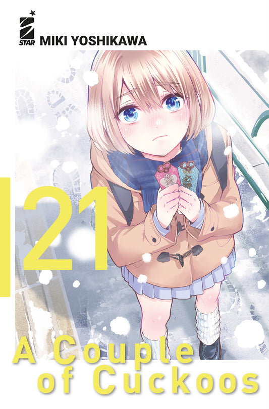 Copertina del manga A Couple of Cuckoos volume 21. L'illustrazione mostra la giovane Sachi con i capelli biondi a caschetto, che indossa un cappotto invernale beige e una sciarpa azzurra, mentre stringe teneramente tra le mani due amuleti portafortuna sotto la neve.