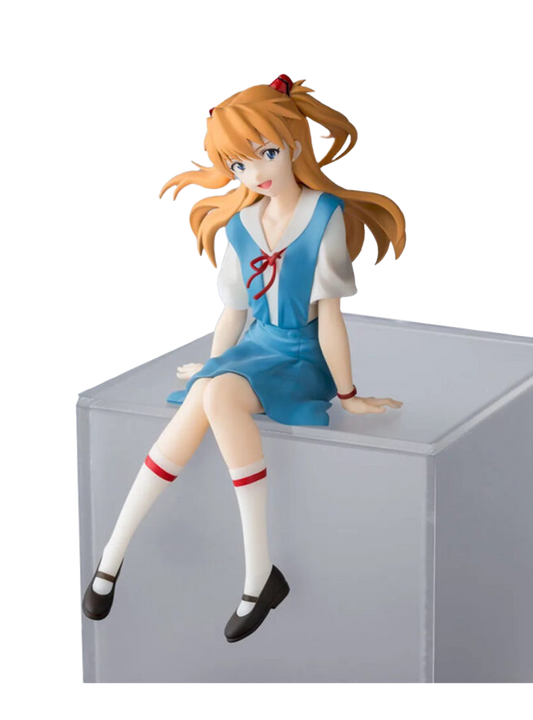 Figura da collezione di Asuka Shikinami Langley prodotta da Sega per la serie Evangelion, mostrata nel file oooo.jpg. La ragazza è seduta in uniforme scolastica azzurra e bianca mentre sorride, con i capelli ramati raccolti nei codini e le gambe che penzolano dal bordo di un cubo trasparente.