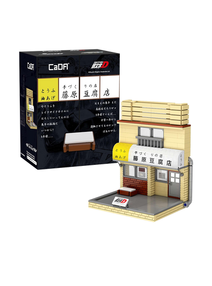 Scatola aperta "a vetrina" con illustrazioni manga di Takumi e Bunta Fujiwara e modellino costruito in mattoncini del negozio Fujiwara Tofu Shop con insegna giapponese e porta scorrevole.