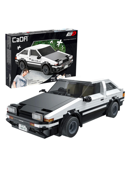 Il modello assemblato in mattoncini bianchi e neri della macchina Toyota AE86 Trueno della serie anime Initial D posizionato in primo piano, con la sua scatola originale CaDA visibile sullo sfondo nero che mostra l'auto in azione e il personaggio di Takumi Fujiwara.
