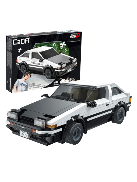 Il modello assemblato in mattoncini bianchi e neri della macchina Toyota AE86 Trueno della serie anime Initial D posizionato in primo piano, con la sua scatola originale CaDA visibile sullo sfondo nero che mostra l'auto in azione e il personaggio di Takumi Fujiwara.
