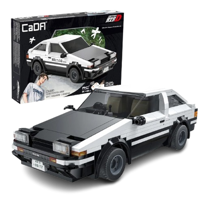Il modello assemblato in mattoncini bianchi e neri della macchina Toyota AE86 Trueno della serie anime Initial D posizionato in primo piano, con la sua scatola originale CaDA visibile sullo sfondo nero che mostra l'auto in azione e il personaggio di Takumi Fujiwara.