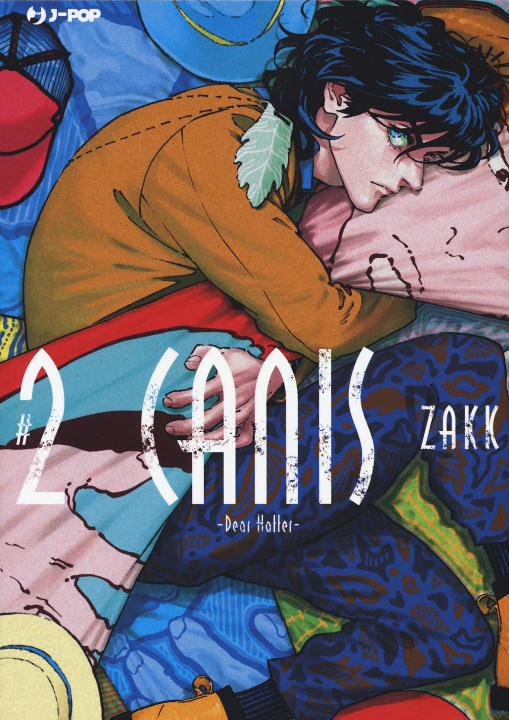 Copertina del secondo volume del manga Boys' Love 'Canis - Dear Hatter -' di ZAKK, edito da J-POP Manga. L'illustrazione ritrae un ragazzo dai capelli scuri e mossi rannicchiato su un cuscino rosa tra variopinti cappelli e stoffe, vestito con una giacca color senape e pantaloni blu a fantasia, sormontato dalla scritta '#2 CANIS -Dear Hatter-' stilizzata in bianco.