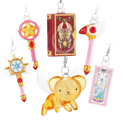 Immagine promozionale dei 6 ciondoli gashapon della collezione Card Captor Sakura Capsule Personal Marker Charm 2 disposti su sfondo bianco. In basso al centro spicca una tenera figure in plastica traslucida color ambra del piccolo leoncino alato Kero-chan. Attorno a lui sono sospesi gli altri cinque ciondoli della serie: a sinistra lo Scettro dei Sogni azzurro e dorato e lo Scettro della Stella rosa e oro; in alto al centro il celebre Libro di Clow rosso scuro con il suo stemma dorato e bianco.