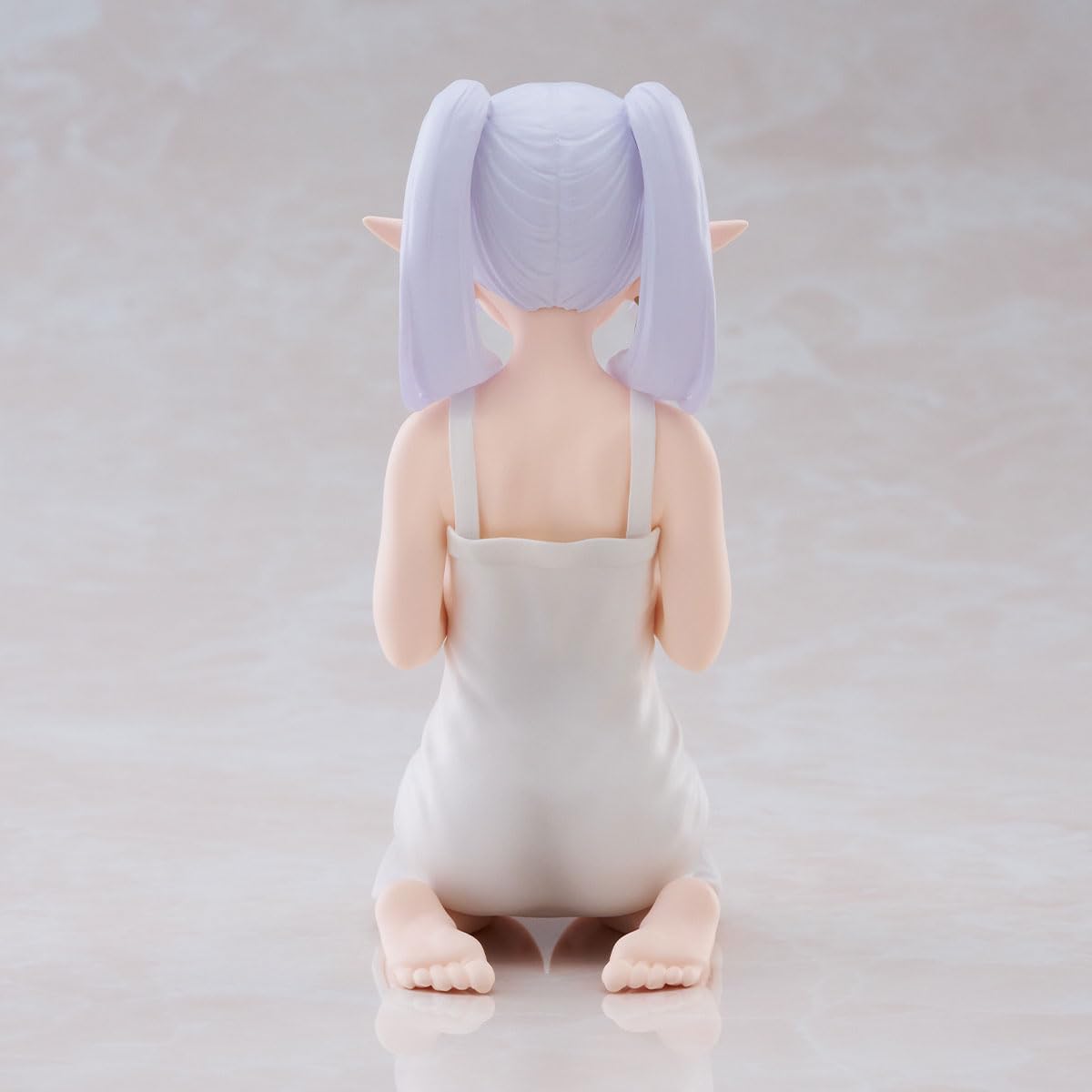 La figure di Frieren della linea Relax Time, inginocchiata in una veste bianca semplice, mentre sorride dolcemente tenendo tra le mani una boccetta viola di pozione.