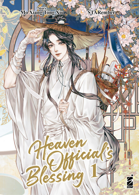 Copertina del manhua Heaven Official's Blessing Vol. 1, edito in Italia da Star Comics. L'illustrazione, dallo stile raffinato e ricco di dettagli, ritrae il protagonista Xie Lian in primo piano. È un giovane uomo affascinante dai lunghi e setosi capelli scuri, vestito con una morbida e candida veste tradizionale bianca. Con una mano, le cui braccia sono avvolte da bende bianche, solleva leggermente un ampio cappello di paglia dalla testa, rivolgendo un sorriso dolce e sereno allo spettatore. Sulle spalle p