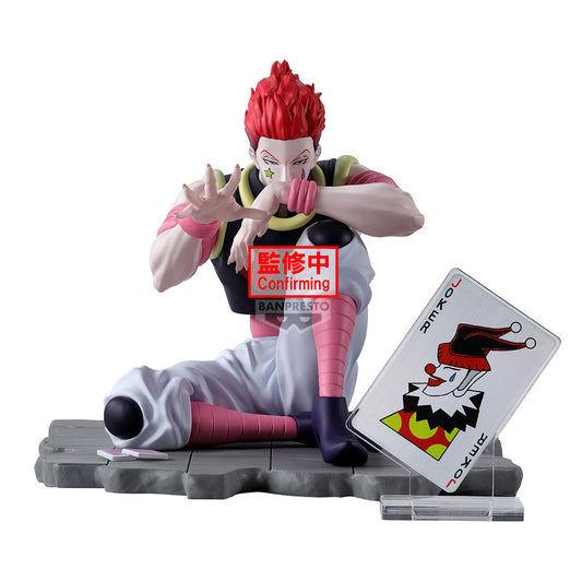 Figure di Hisoka da Hunter x Hunter seduto a gambe incrociate su una base grigia; ha capelli rossi e indossa il suo costume tipico. Accanto a lui c'è una grande carta da gioco del Joker.