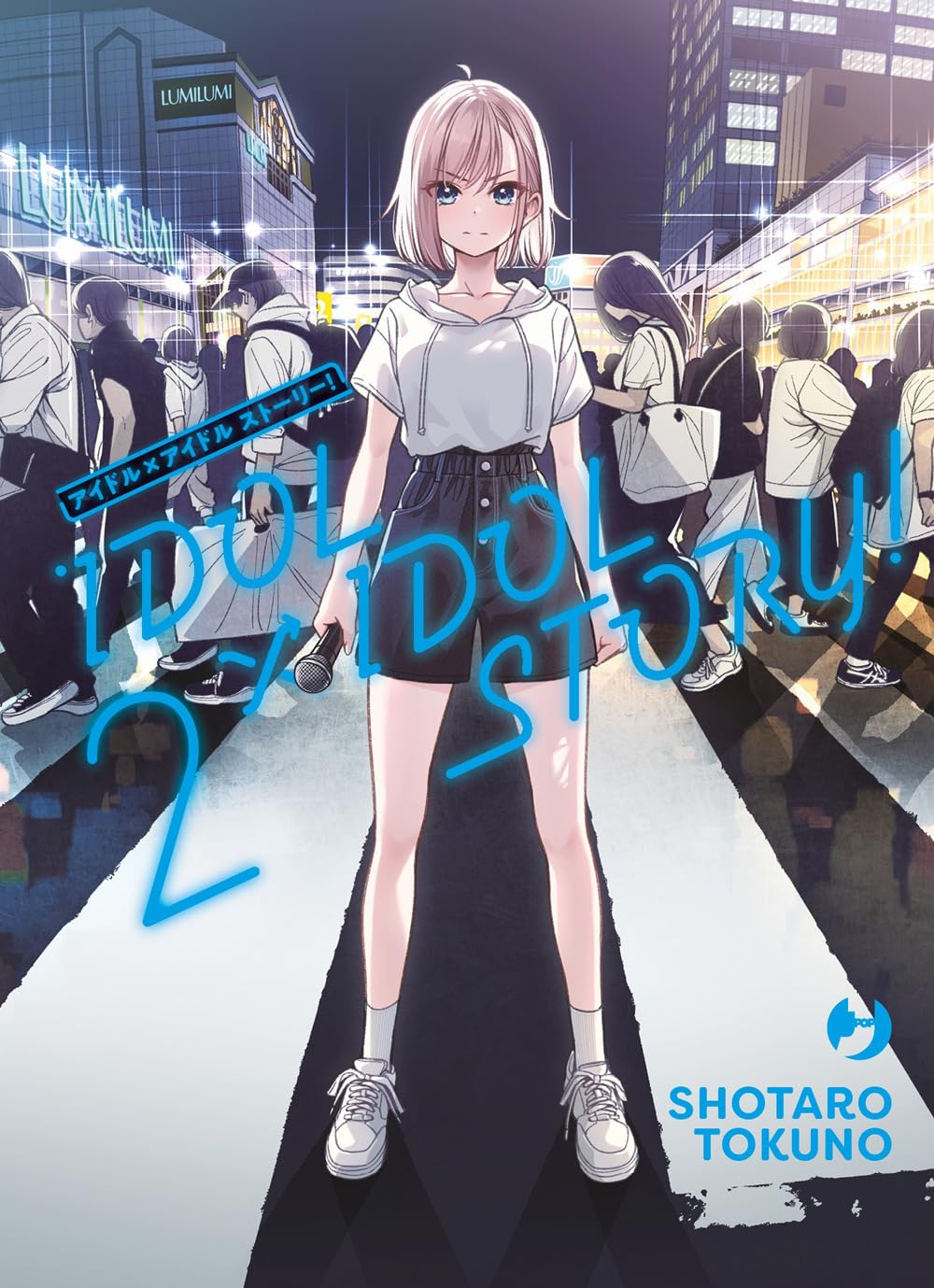Copertina del secondo volume del manga Idol x Idol Story!. Al centro campeggia una ragazza con capelli corti biondo-rosati, che indossa una felpa bianca a mezze maniche e pantaloncini neri mentre stringe un microfono, ferma in mezzo a un affollato incrocio cittadino illuminato di notte.