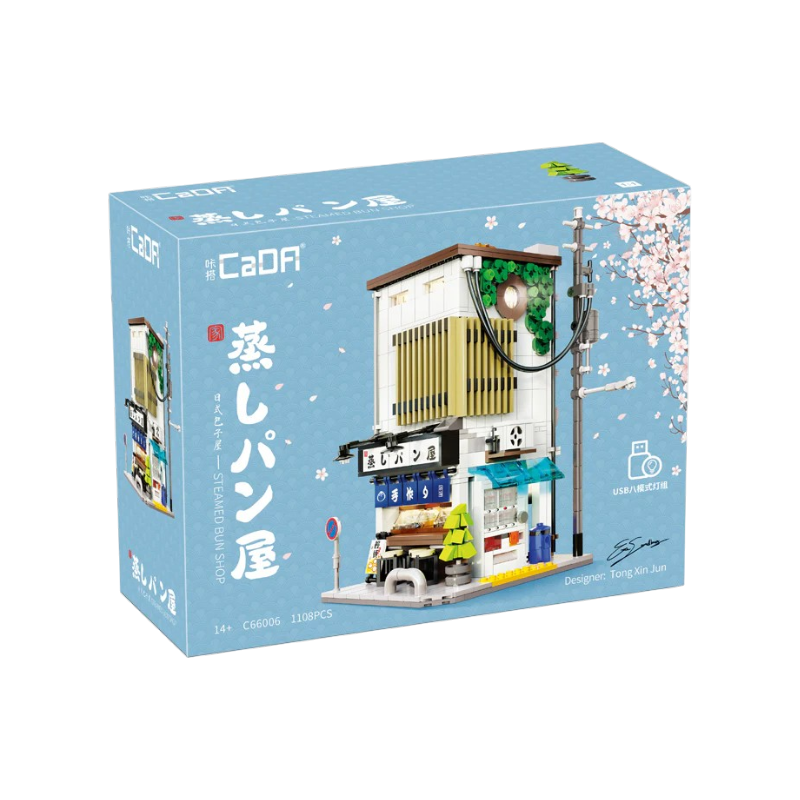 Scatola del kit di costruzioni CaDA Japanese Stuffed Bun House. Al centro è raffigurato il modello assemblato di un tradizionale negozio giapponese a due piani, affiancato da un palo della luce, su uno sfondo celeste decorato con delicati fiori di ciliegio.
