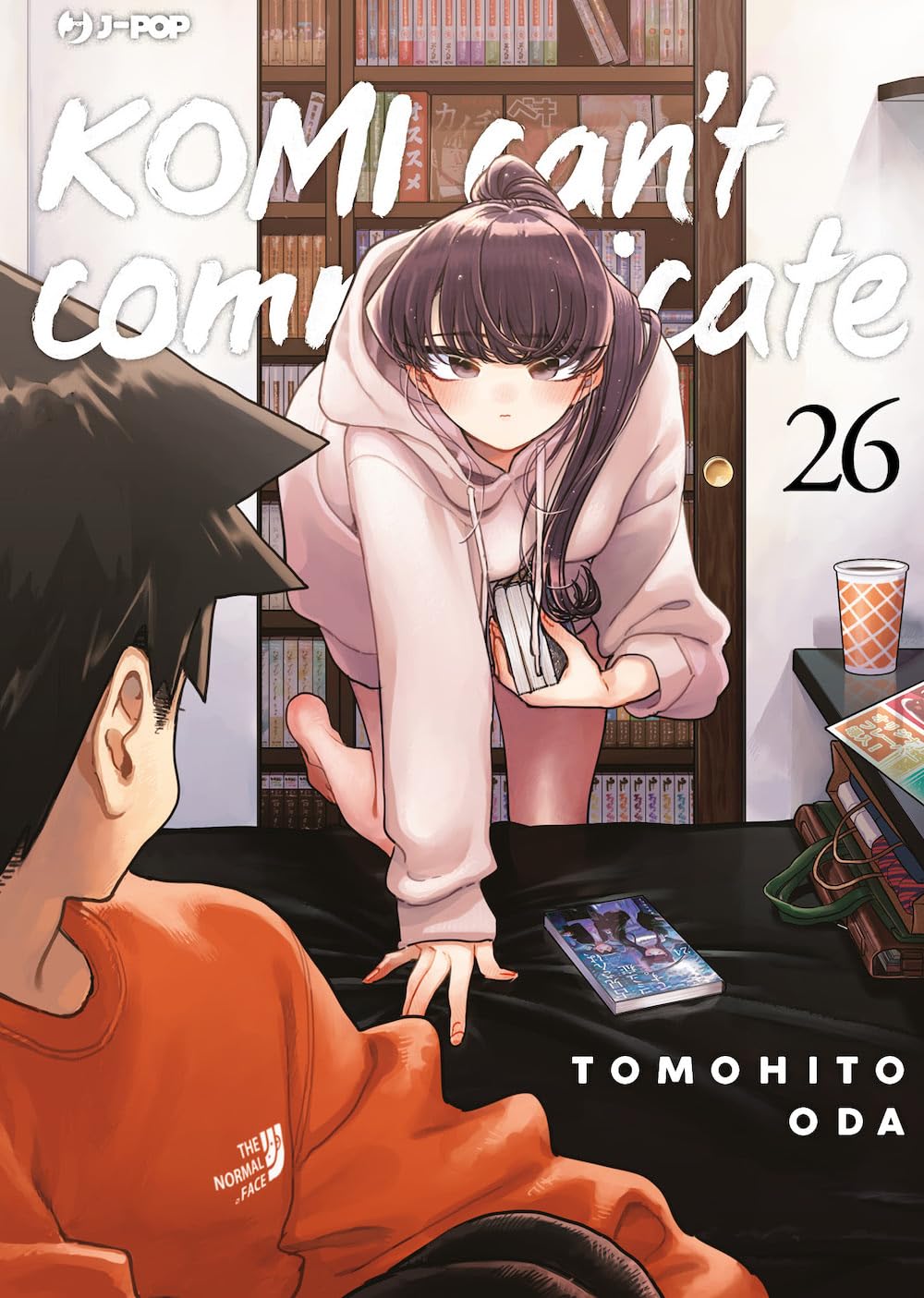 Copertina del ventiseiesimo volume del manga 'Komi Can't Communicate' di Tomohito Oda, edito da J-POP Manga. L'illustrazione ritrae la protagonista Shouko Komi con i capelli raccolti e in felpa chiara mentre si sporge in avanti verso Tadano (in felpa arancione, visto di spalle) all'interno di un privato box di un manga café con librerie sullo sfondo, sormontata dal titolo in bianco e dal numero 26 sulla destra.