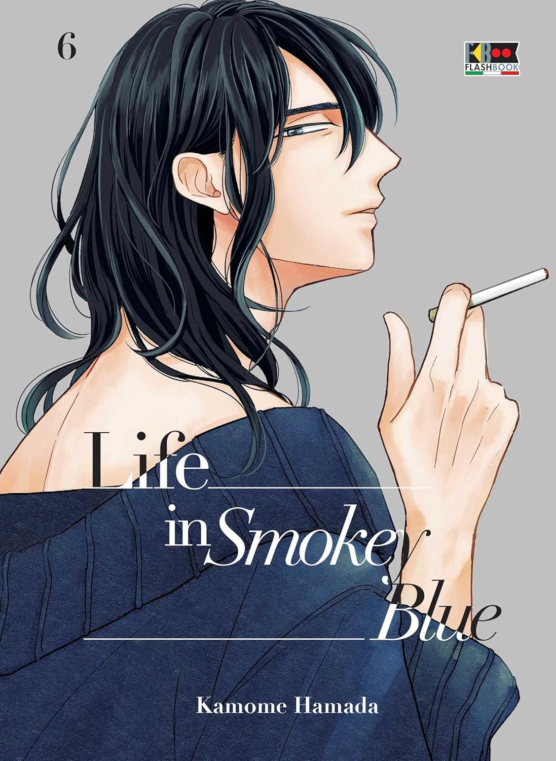 Copertina del manga Life in Smokey Blue Vol. 6. Illustrazione elegante che ritrae di profilo un ragazzo dai lunghi capelli scuri. Indossa un maglione blu scuro scivolato su una spalla, tenendo con delicatezza una sigaretta accesa nella mano destra. Lo sfondo è di un colore grigio chiaro e neutro, con il titolo dell'opera scritto al centro e il nome dell'autrice, Kamome Hamada, in basso.