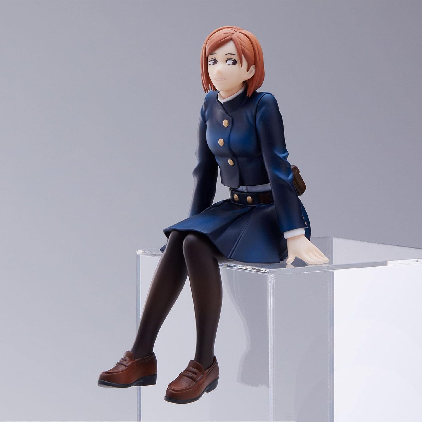 Figure da collezione in PVC di Nobara Kugisaki dalla serie anime 'Jujutsu Kaisen', prodotta da Sega. La statuetta ritrae la giovane strega seduta su un blocco trasparente con la classica uniforme blu scuro della scuola di stregoneria di Tokyo, gonna a pieghe, calze nere, mocassini marroni e corti capelli castano-ramati.