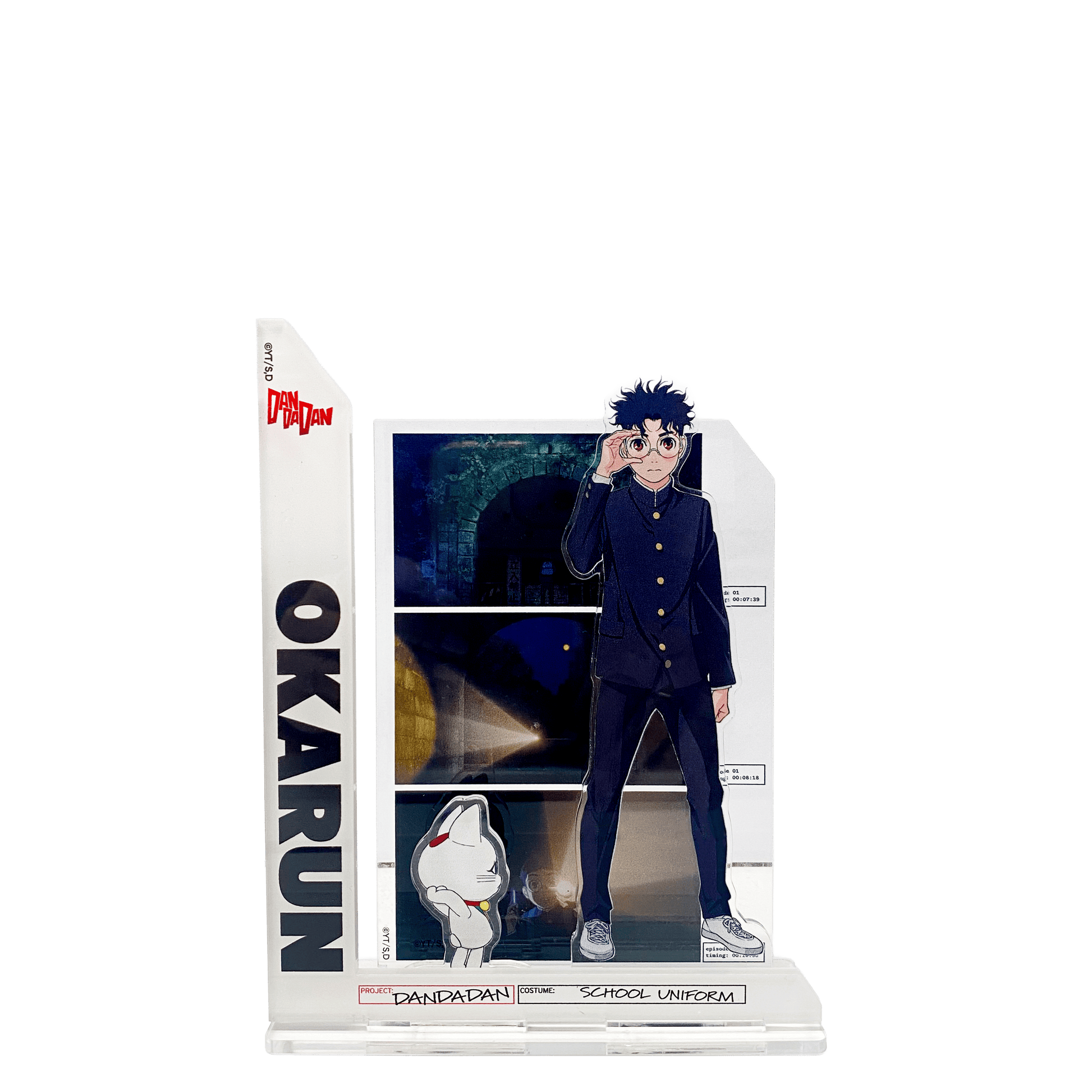 Acrylic standee composto da più parti assemblate: al centro il personaggio Okarun in divisa scolastica nera che si tocca gli occhiali; a sinistra una barra verticale con la scritta "OKARUN"; in basso una piccola figura della Turbo Granny in forma di gatto bianco; sullo sfondo un pannello rettangolare con scene scure tratte dall'anime/manga.