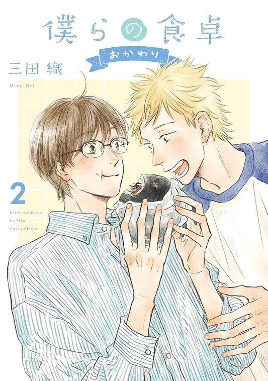 Copertina del manga Our Dining Table Facciamo il Bis Vol. 2; Yutaka, con capelli castani e occhiali, tiene in mano un onigiri nero che Minoru, biondo e sorridente, sta addentando; stile acquerello su sfondo chiaro.