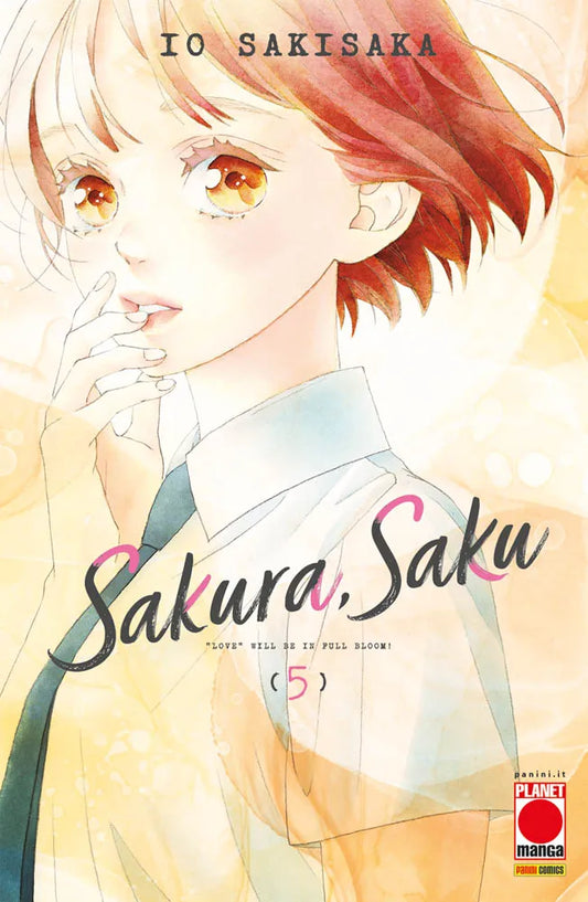 Copertina del quinto volume in italiano del manga shojo 'Sakura, Saku' di Io Sakisaka, edito da Panini Planet Manga. L'illustrazione ad acquarello dai toni caldi e luminosi mostra in primo piano la protagonista Saku Fujisaki con brevi capelli ramati, grandi occhi ambrati e divisa scolastica con cravatta scura, mentre si porta pensierosa le dita alle labbra. Al centro figura il titolo 'Sakura, Saku' scritto in un elegante corsivo nero con dettagli rosa, la frase '"LOVE" WILL BE IN FULL BLOOM!'.