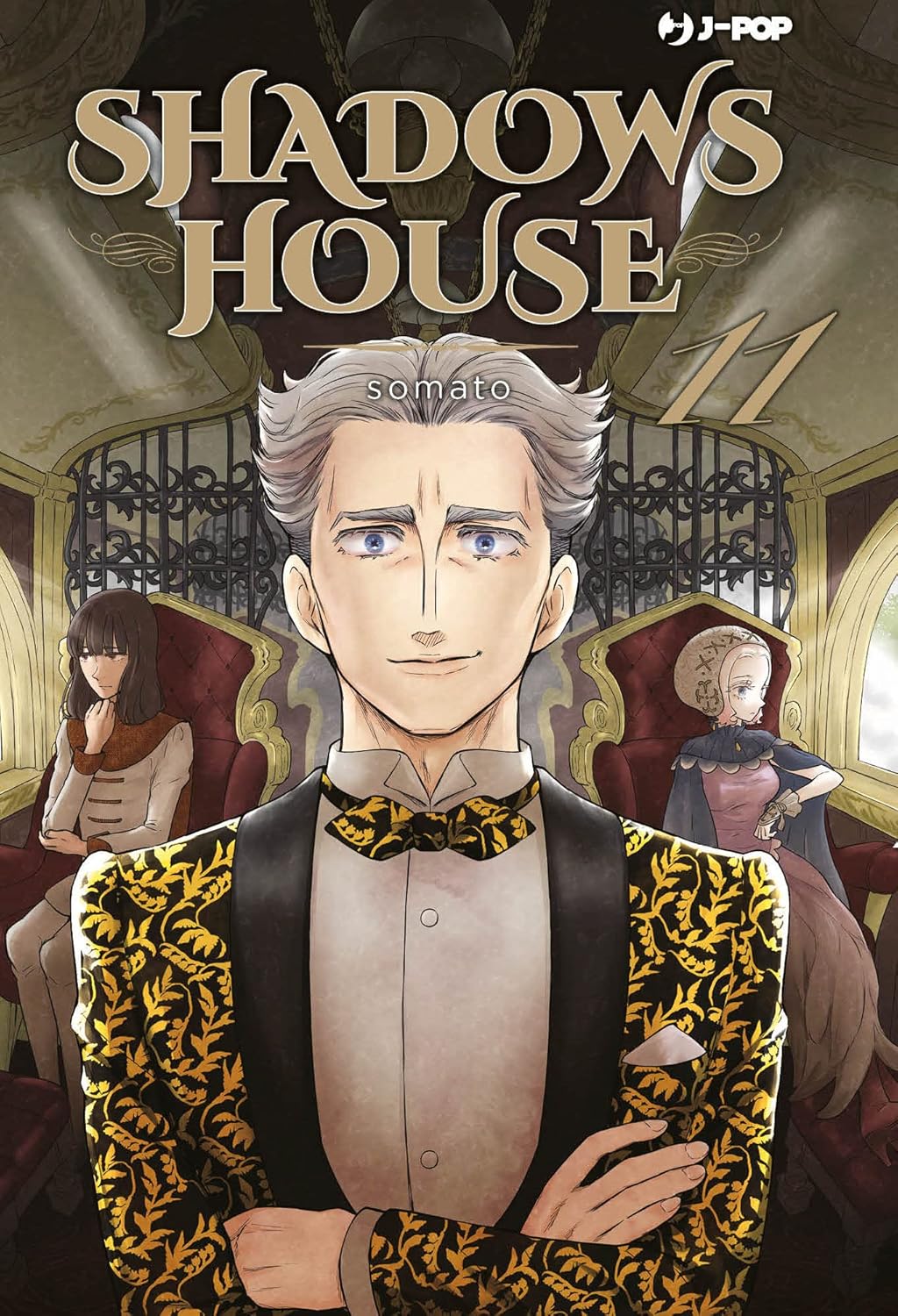 Copertina del manga Shadows House Vol. 11 edito da J-Pop. In primo piano troneggia l'enigmatico personaggio di Edward, l'esaminatore, ritratto con un mezzo sorriso e uno sguardo penetrante. Indossa un'elegante giacca damascata oro e nera con un farfallino coordinato. Alle sue spalle, sedute su poltrone di velluto rosso, si vedono altre due figure femminili in abiti nobiliari. In alto a destra risalta il numero 11.