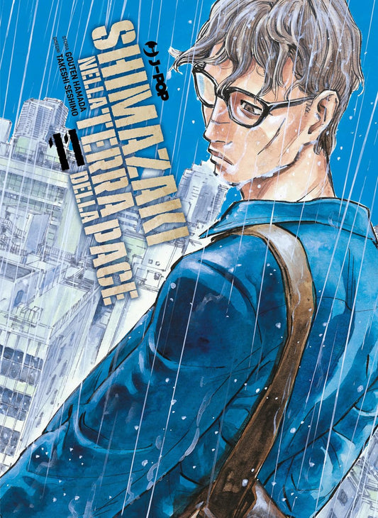 Copertina dell'undicesimo volume del manga 'Shimazaki nella Terra Della Pace' di Gouten Hamada e Takeshi Seshimo, edito da J-POP Manga. L'illustrazione ritrae in primo piano e di tre quarti il protagonista Shingo Shimazaki mentre cammina sotto la pioggia battente, con occhiali da vista, giacca blu e borsa a tracolla su uno sfondo urbano di palazzi, affiancato dal titolo 'SHIMAZAKI NELLA TERRA DELLA PACE', dal numero 11, dal logo J-POP e dai nomi degli autori in alto a sinistra.   