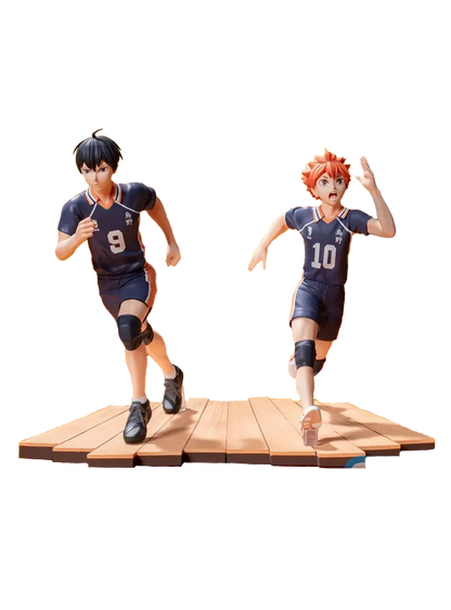 Due figure da collezione dei personaggi Shoyo Hinata e Tobio Kageyama dall'anime Haikyu!!. I due ragazzi, uno con capelli arancioni e il numero 10 e l'altro con capelli neri e il numero 9, indossano divise da pallavolo scure e sono ritratti mentre corrono con espressioni decise su una base che riproduce il parquet di una palestra.