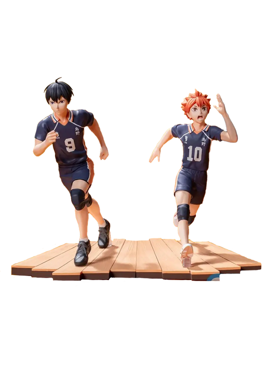 Due figure da collezione dei personaggi Shoyo Hinata e Tobio Kageyama dall'anime Haikyu!!. I due ragazzi, uno con capelli arancioni e il numero 10 e l'altro con capelli neri e il numero 9, indossano divise da pallavolo scure e sono ritratti mentre corrono con espressioni decise su una base che riproduce il parquet di una palestra.