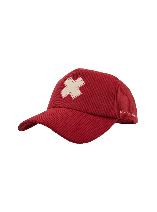 Cappellino con visiera in stile baseball, realizzato in tessuto a coste di colore rosso. Sulla parte frontale è applicata una toppa a forma di croce bianca a forma di X con finta cucitura a contrasto sui bordi. Sul lato sinistro della calotta è presente un ricamo bianco con caratteri giapponesi. Il design è ispirato a Tony Tony Chopper di One Piece.